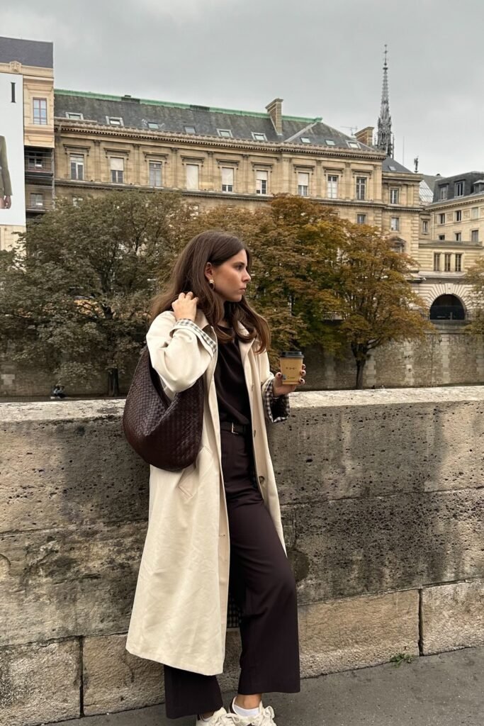 Beige Long Trench Coat + Dark Brown Turtleneck + Dark Brown Wide-Leg Trousers + White Sneakers + Brown Woven Shoulder Bag