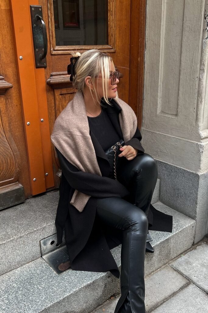 Black Long Coat + Black Sweater + Black Leather Pants + Beige Knit Scarf Draped Over Shoulders + Black Quilted Handbag + Sunglasses