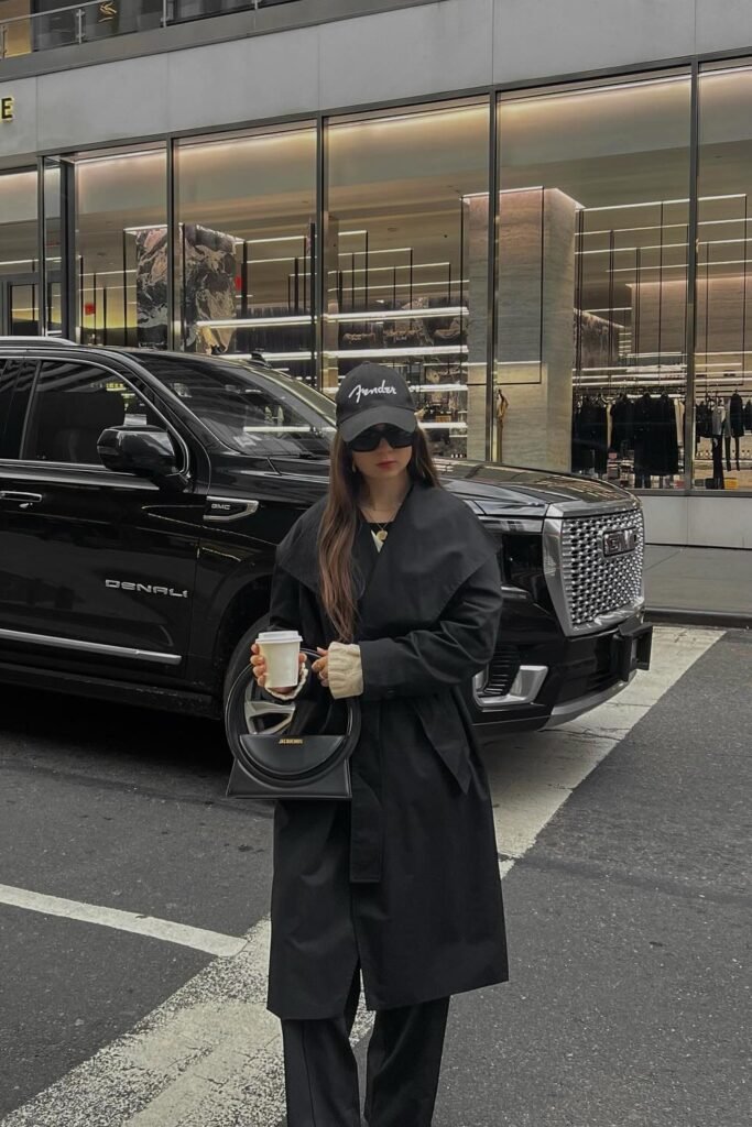 Black Trench Coat + Black Wide-Leg Trousers + Beige Knit Cuffs Peeking + Black Baseball Cap + Structured Black Top-Handle Bag