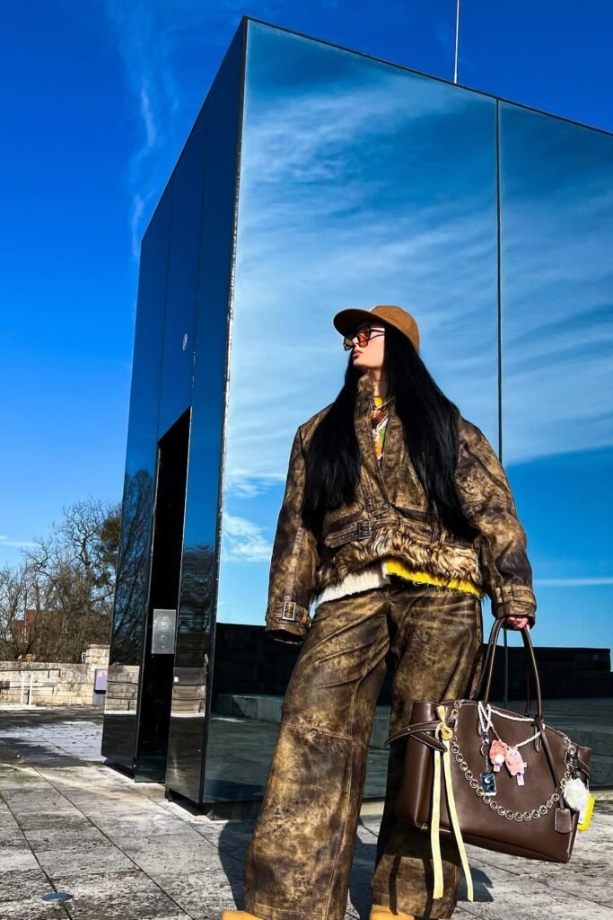 Brown Distressed Oversized Jacket with Fur Trim + Brown Wide-Leg Pants + Brown Baseball Cap + Large Brown Tote with Keychains + Yellow Layered Knit Detail