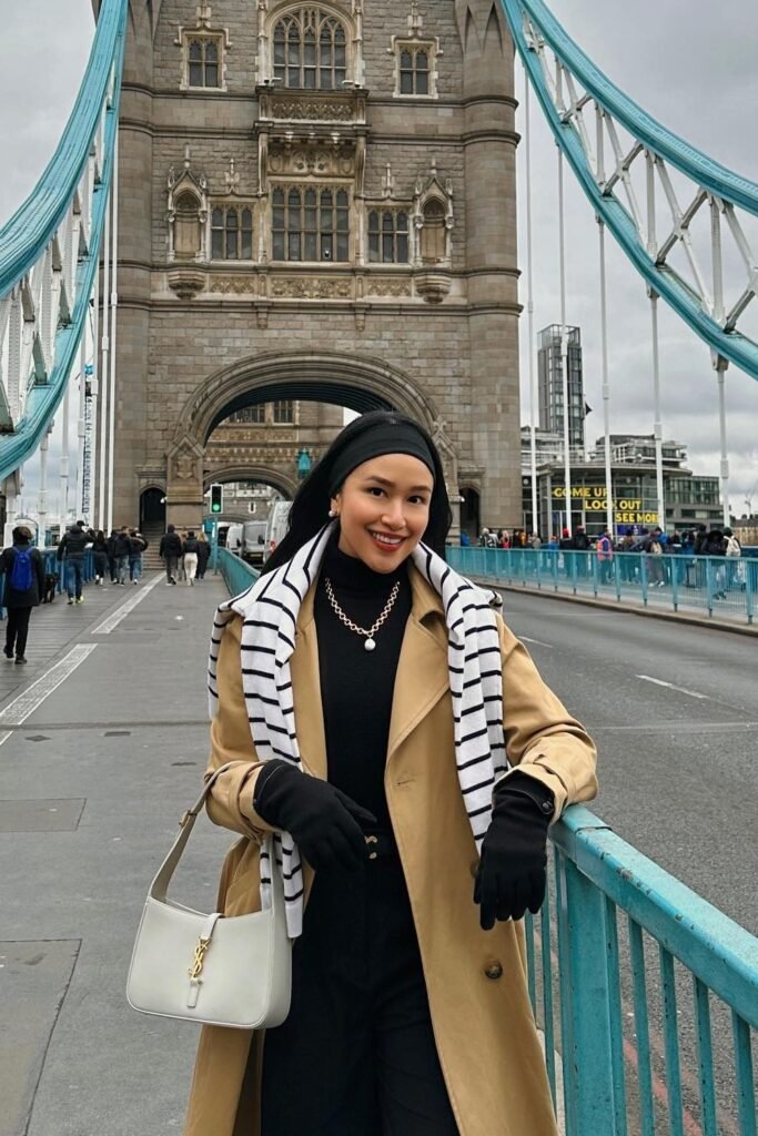 Camel Trench Coat + Black Turtleneck + Black Trousers + Striped Sweater Draped Over Shoulders + White Shoulder Bag + Black Gloves