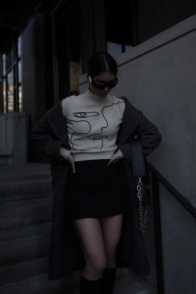 Grey Long Coat + Abstract Face Print Sweater + Black Mini Skirt + Black Knee-High Boots + Black Shoulder Bag