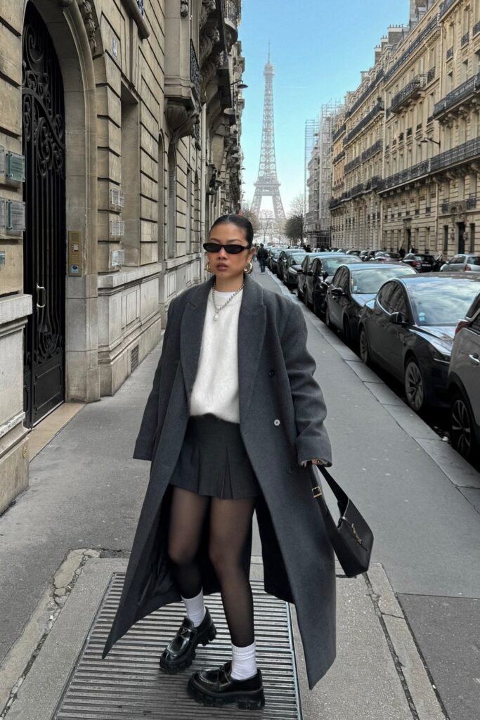 Grey Oversized Wool Coat + White Fluffy Sweater + Grey Pleated Mini Skirt + Black Chunky Loafers with White Socks + Black Structured Bag + Black Slim Sunglasses