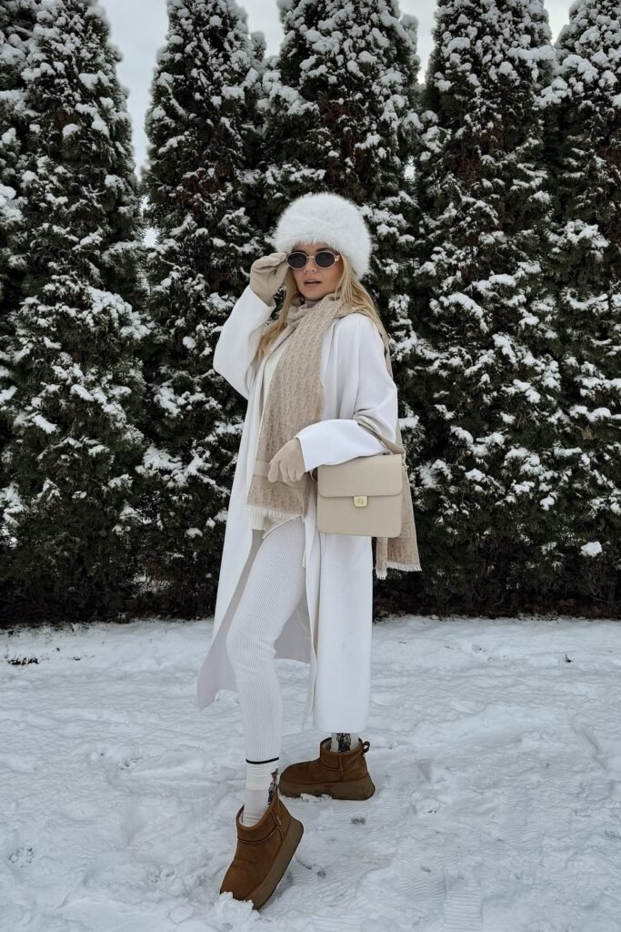 White Long Coat + Beige Scarf + White Knit Top + White Leggings + Brown Ugg Boots + White Fur Hat + Beige Shoulder Bag + Sunglasses
