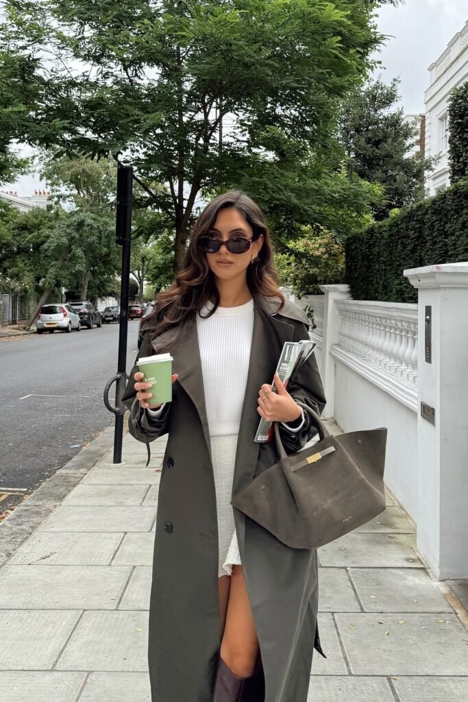 Olive Green Trench Coat + White Ribbed Sweater + White Mini Skirt + Dark Brown Knee-High Boots + Oversized Brown Tote Bag