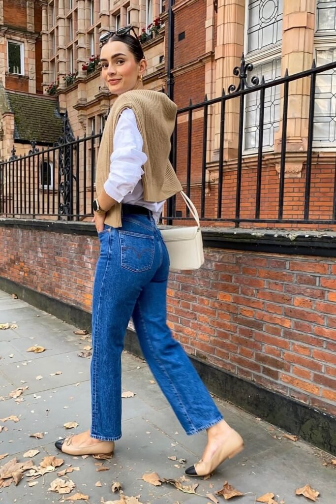 White Button-Up Shirt + Beige Sweater Draped Over Shoulders + Blue Straight-Leg Jeans + Beige Cap-Toe Flats + White Structured Bag
