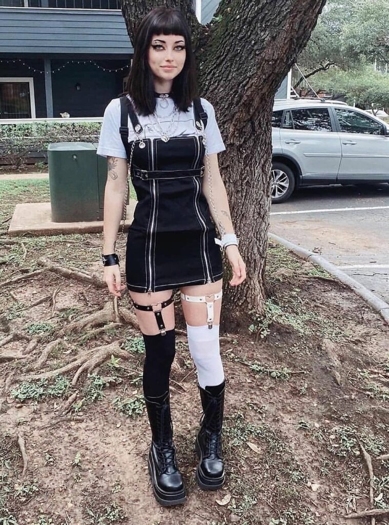 White T-shirt + Black Buckle Strap Mini Dress + Black & White Mismatched Thigh-High Socks with Harness + Black Platform Combat Boots + Layered Chains