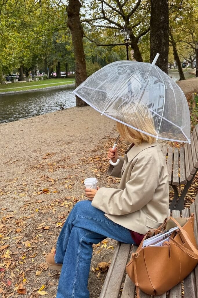 Beige Short Trench Coat + Burgundy Sweater + Wide-Leg Jeans + Tan Boots + Clear Umbrella