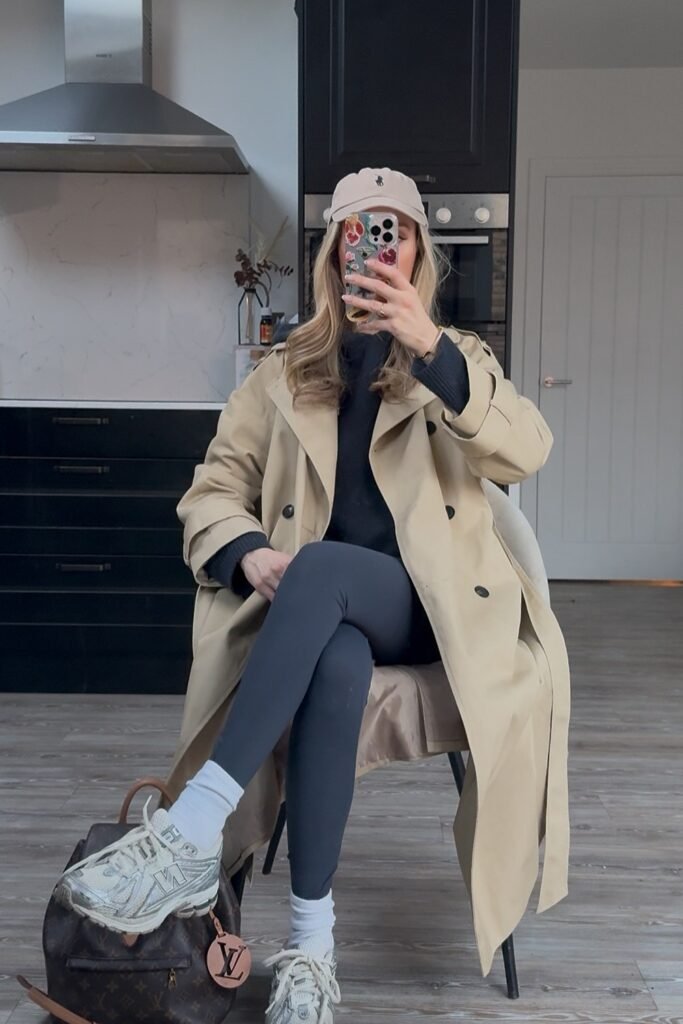 Beige Trench Coat + Black Top + Dark Grey Leggings + Beige Cap + White/Silver Sneakers