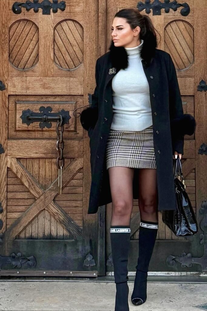 Black Coat with Faux Fur Trim + White Turtleneck Sweater + Plaid Mini Skirt + Black Knee-High Logo Socks + Black Boots