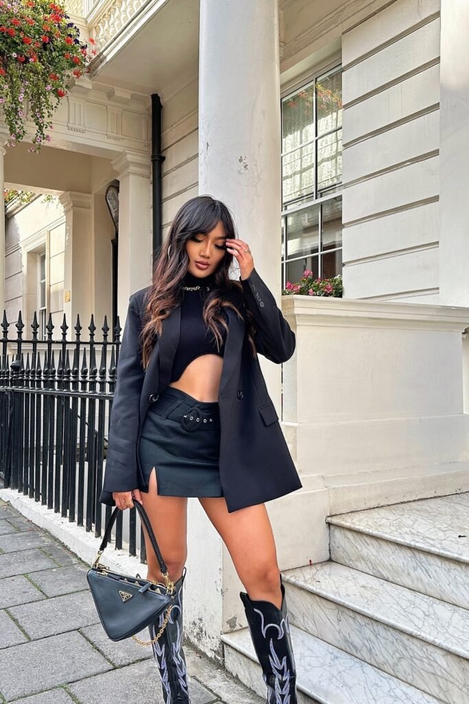 Black Cropped Knit Top + Black Mini Skirt with Slit + Black Oversized Blazer + Black Knee-High Cowboy Boots + Black Handbag
