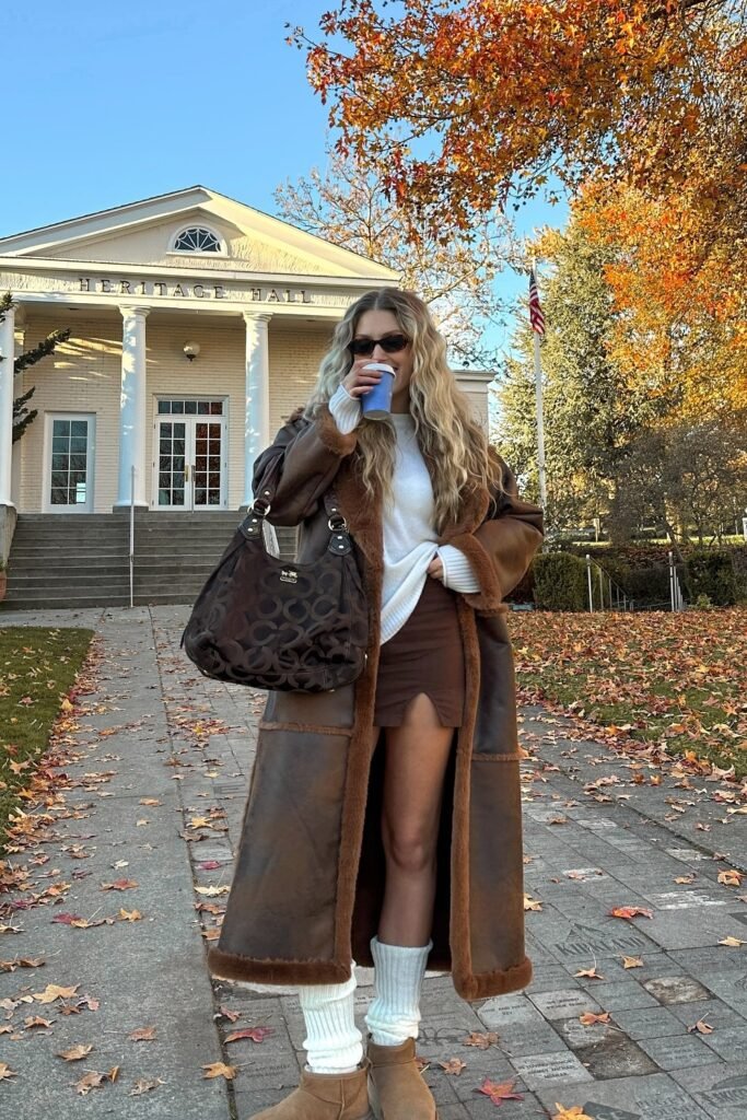 Brown Faux Shearling Long Coat + White Sweater + Brown Mini Skirt + Tan Boots + White Leg Warmers