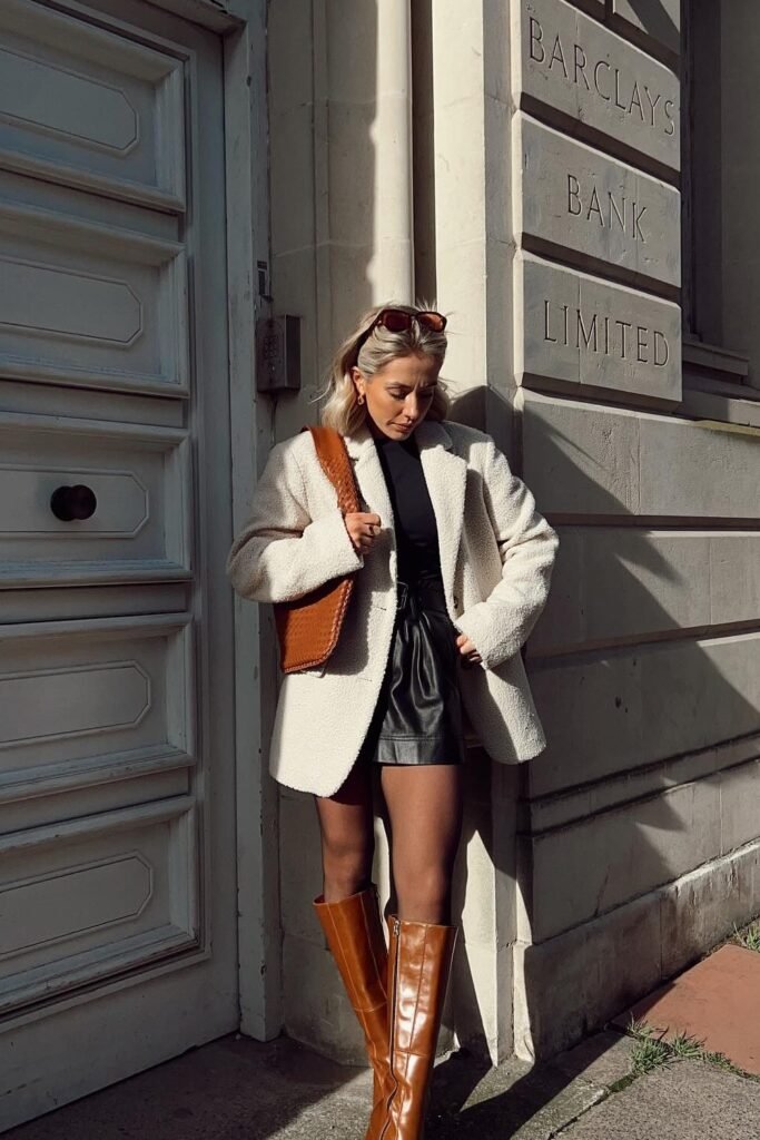 Cream Teddy Blazer + Black Turtleneck + Black Faux Leather Shorts + Brown Knee-High Boots + Brown Woven Bag