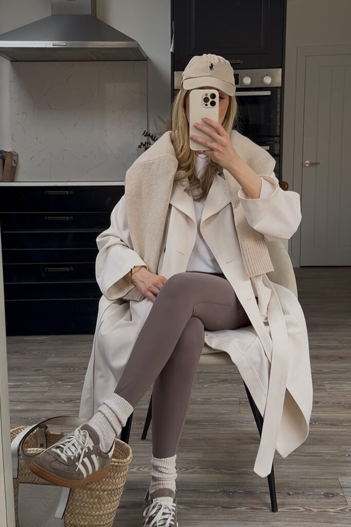 Cream Trench Coat + White T-shirt + Brown Leggings + Taupe Baseball Cap + Adidas Sneakers with Striped Socks