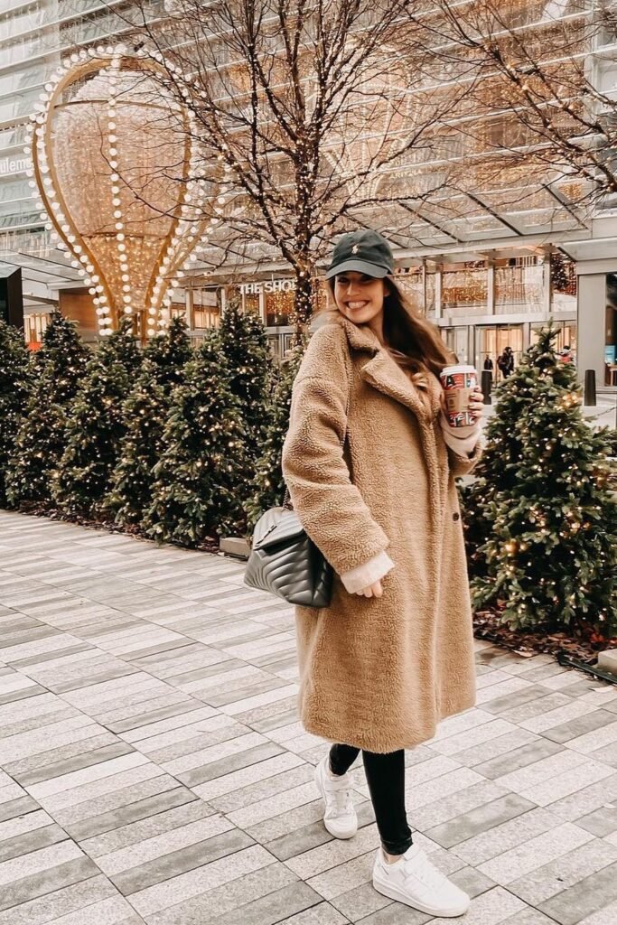 Long Tan Teddy Coat + Light Sweater + Black Leggings + White Sneakers + Dark Baseball Cap