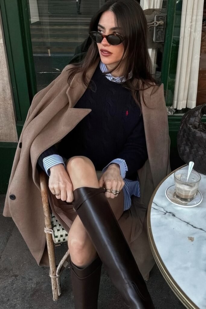 Tan Long Coat + Navy Polo Sweater + Blue and White Striped Collared Shirt + Dark Brown Riding Boots + Cat-Eye Sunglasses