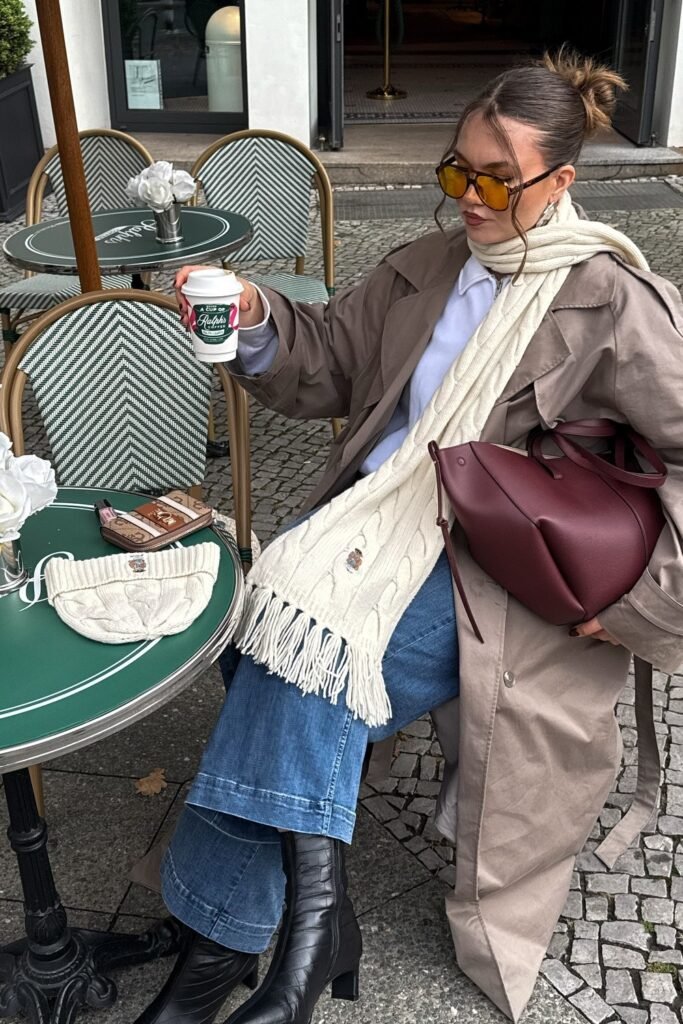 Tan Trench Coat + Light Blue Shirt + Wide-Leg Denim Jeans + Cream Cable Knit Scarf + Black Heeled Ankle Boots + Burgundy Tote Bag