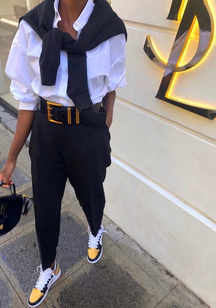 White Button-Down Shirt + Black Trousers + Black Sweater Tied Over Shoulders + Black and Yellow Sneakers