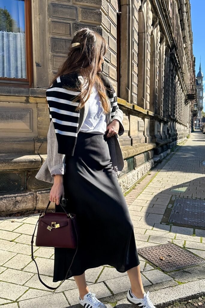 White Ruffled Blouse + Black Satin Maxi Skirt + Black-and-White Striped Sweater (draped) + Burgundy Handbag + White Sneakers