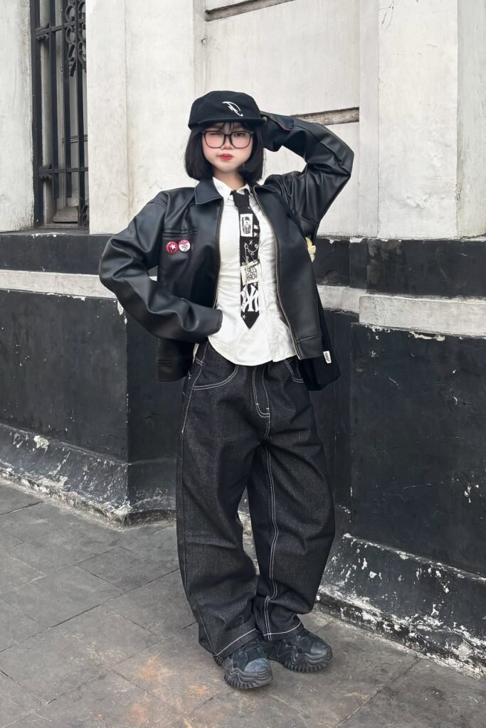 Black Leather Jacket + White Button-Up with Graphic Tie + Baggy Black Contrast-Stitch Jeans + Chunky Black Sneakers + Black Newsboy Cap