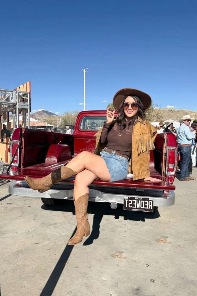 Brown Suede Fringe Jacket + Brown Long-Sleeve Top + Denim Shorts + Tan Cowboy Boots + Brown Wide-Brim Hat