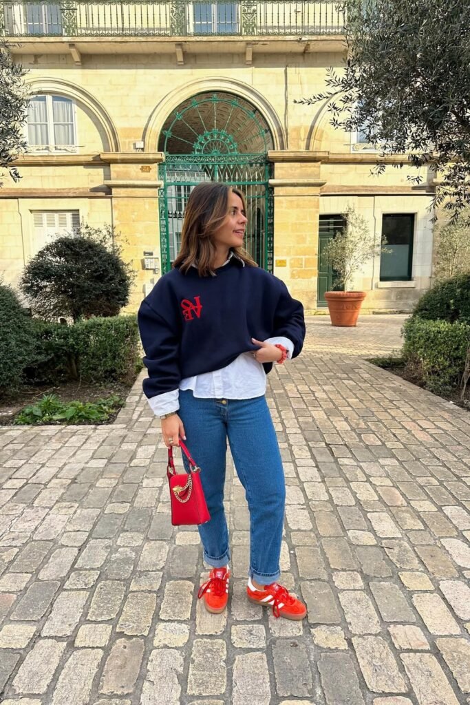 Navy Graphic Sweatshirt + White Collared Shirt + Blue Straight-Leg Jeans + Red Gazelle Sneakers