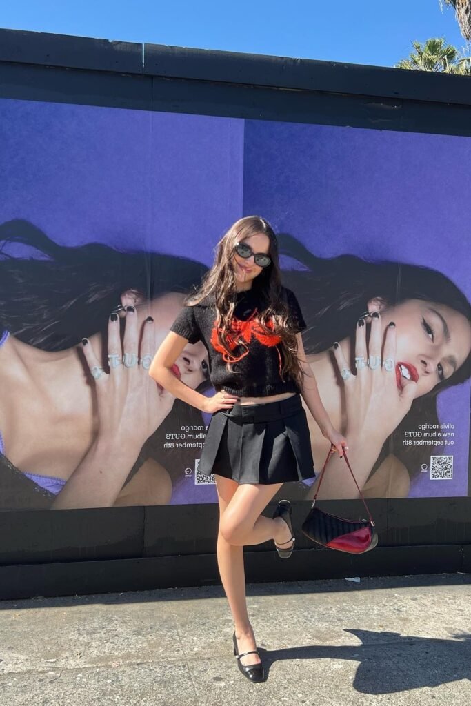 Black Graphic Baby Tee + Black Pleated Mini Skirt + Black Mary Jane Flats + Red and Black Shoulder Bag