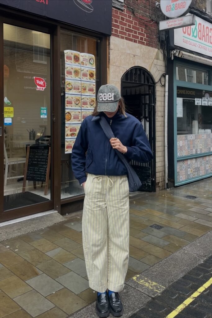Navy Bomber Jacket + Yellow Pinstripe Wide-Leg Pants + Grey Graphic Baseball Cap + Black Loafers