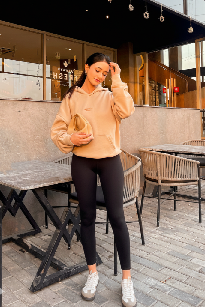 Tan Oversized Hoodie + Black Leggings + White and Grey Sneakers + Tan Clutch Bag