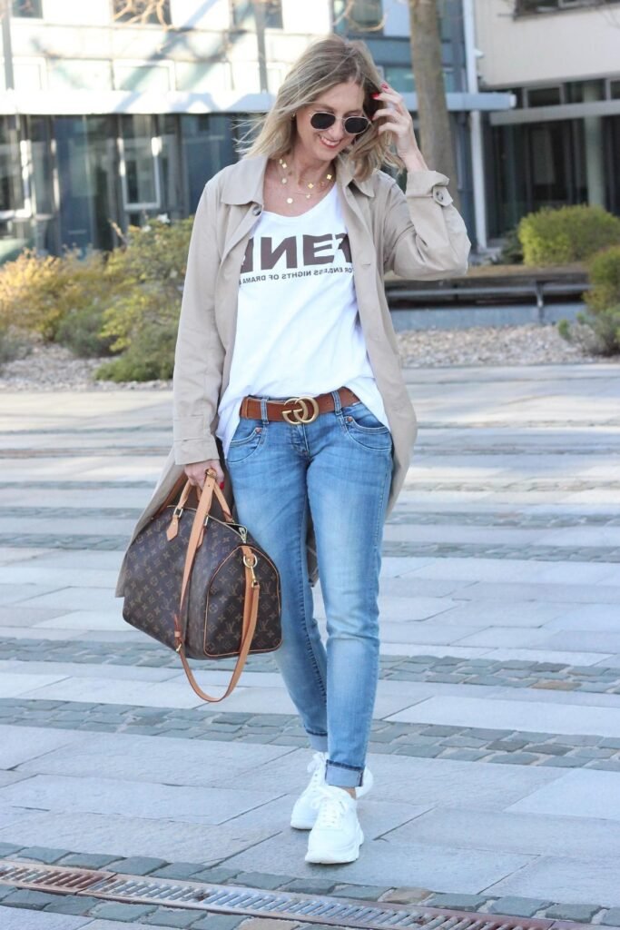 Tan Trench Coat + White Graphic T-Shirt + Light Wash Skinny Jeans + White Chunky Sneakers