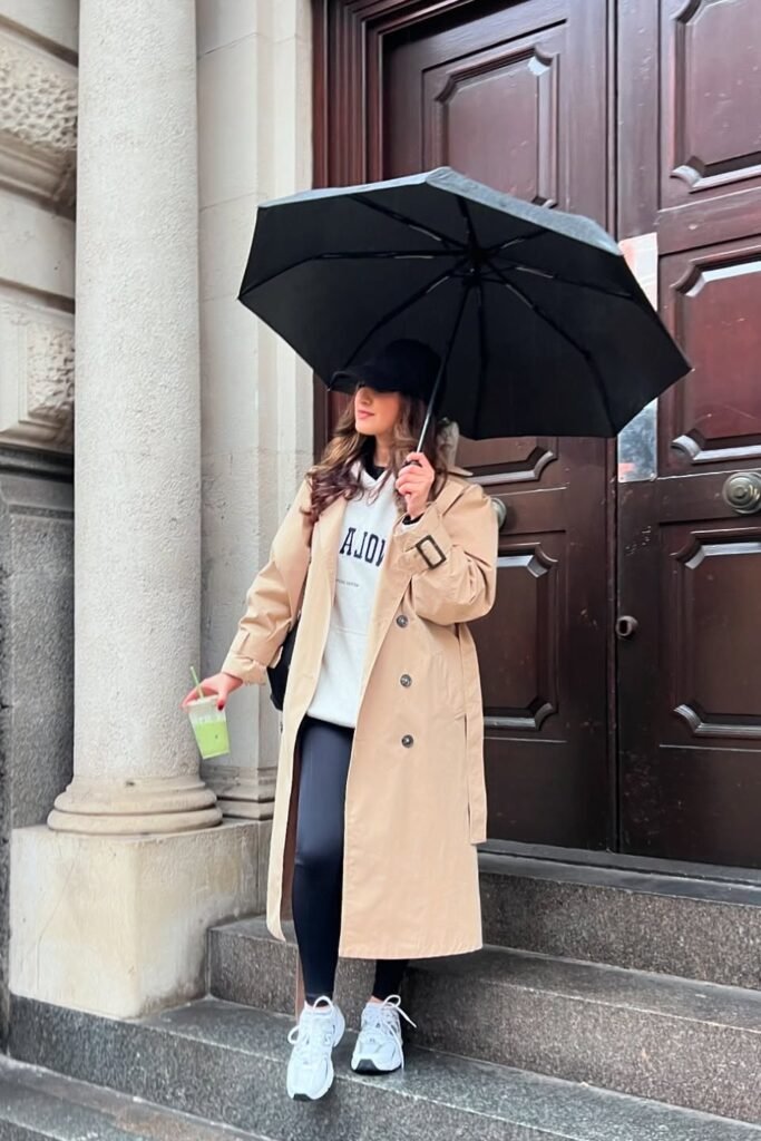 White Graphic Hoodie + Tan Long Trench Coat + Black Leggings + White Athletic Sneakers