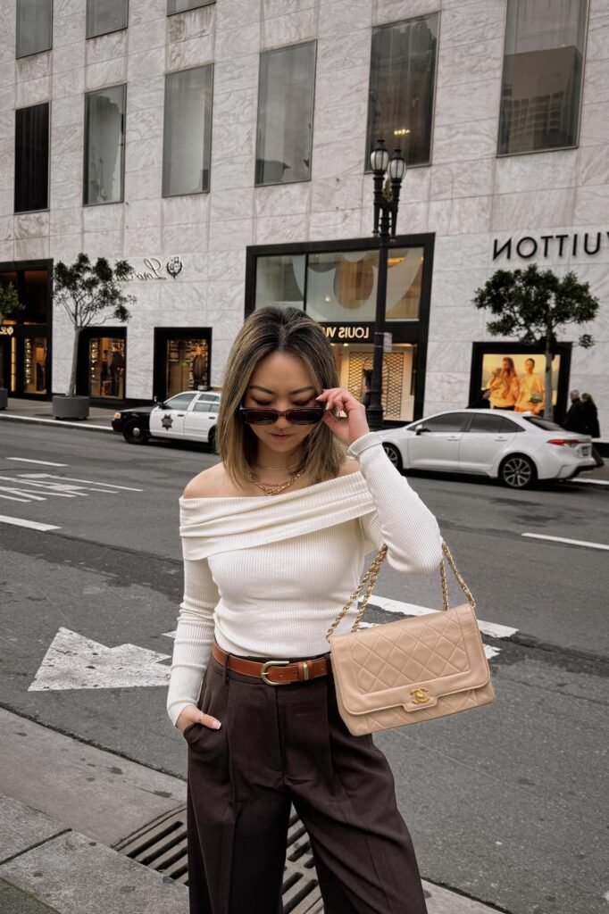 White Off-the-Shoulder Ribbed Sweater + Dark Brown Pleated Trousers + Tan Quilted Chain Bag