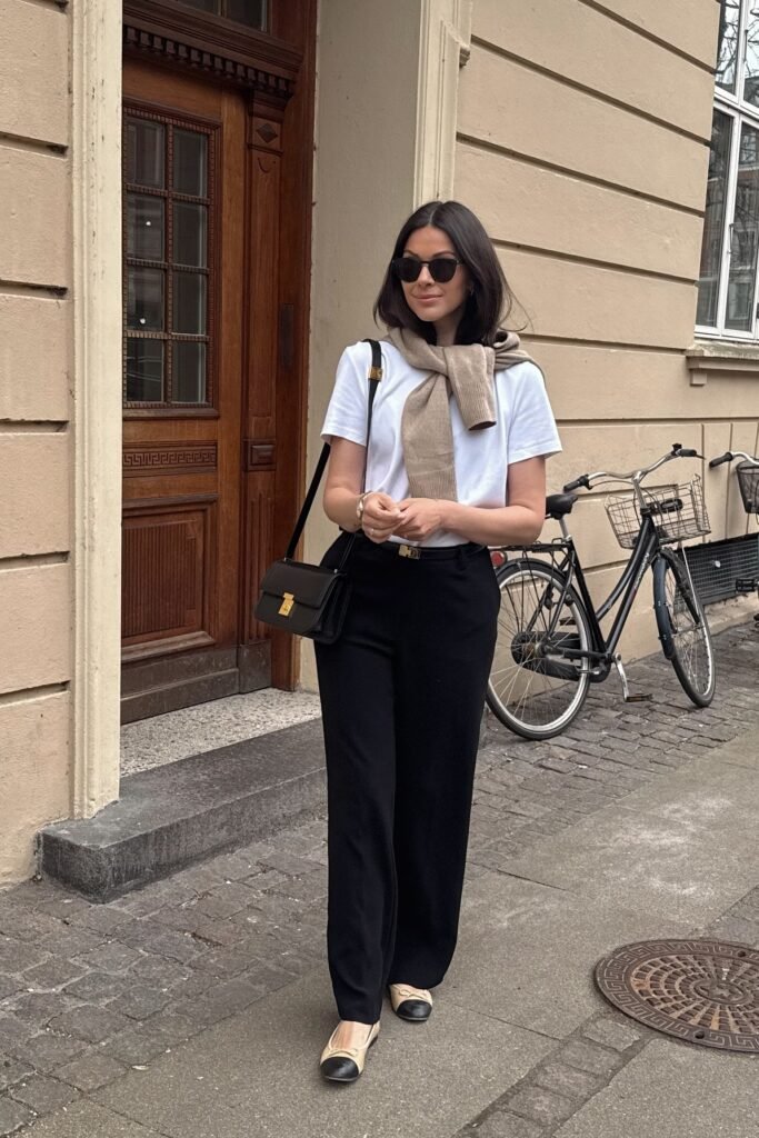 White T-Shirt + Beige Sweater (Draped over shoulders) + Black Straight-Leg Trousers + Beige and Black Cap-Toe Ballet Flats