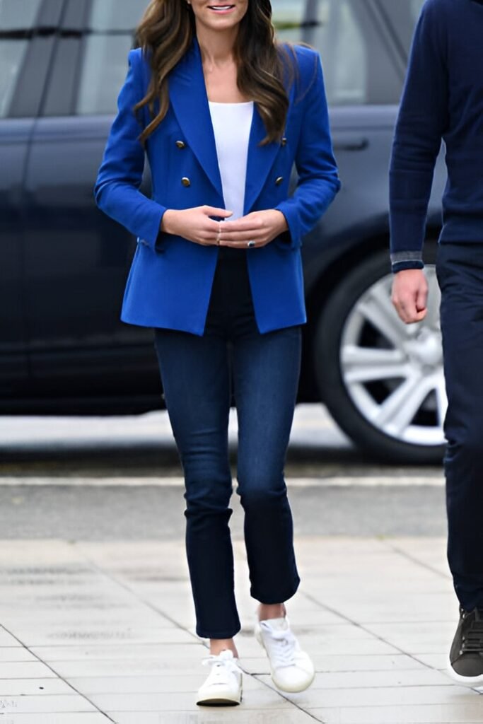 Woman wearing a stylish casual brunch outfit: a royal blue blazer over a white top with dark cropped jeans and white sneakers, perfect for a cafe.