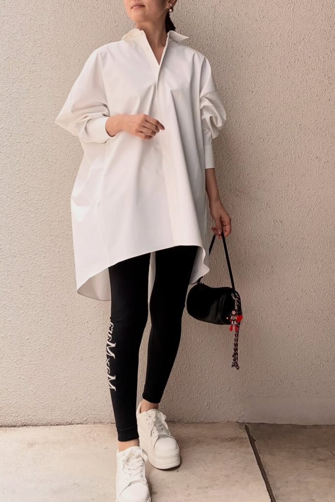 Comfortable and chic brunch athleisure outfit with an oversized white button-down tunic, black leggings, and white platform sneakers.