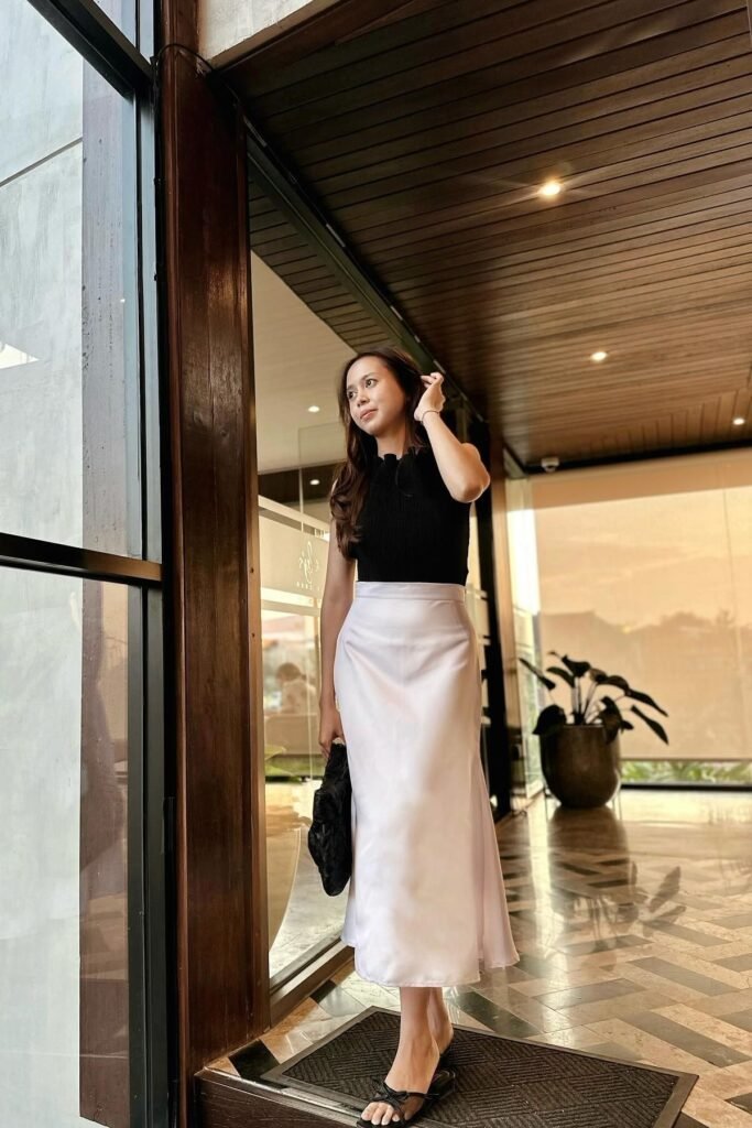 Trendy day party brunch outfit combining a black sleeveless knit top with a luxurious white satin midi skirt and strappy sandals.