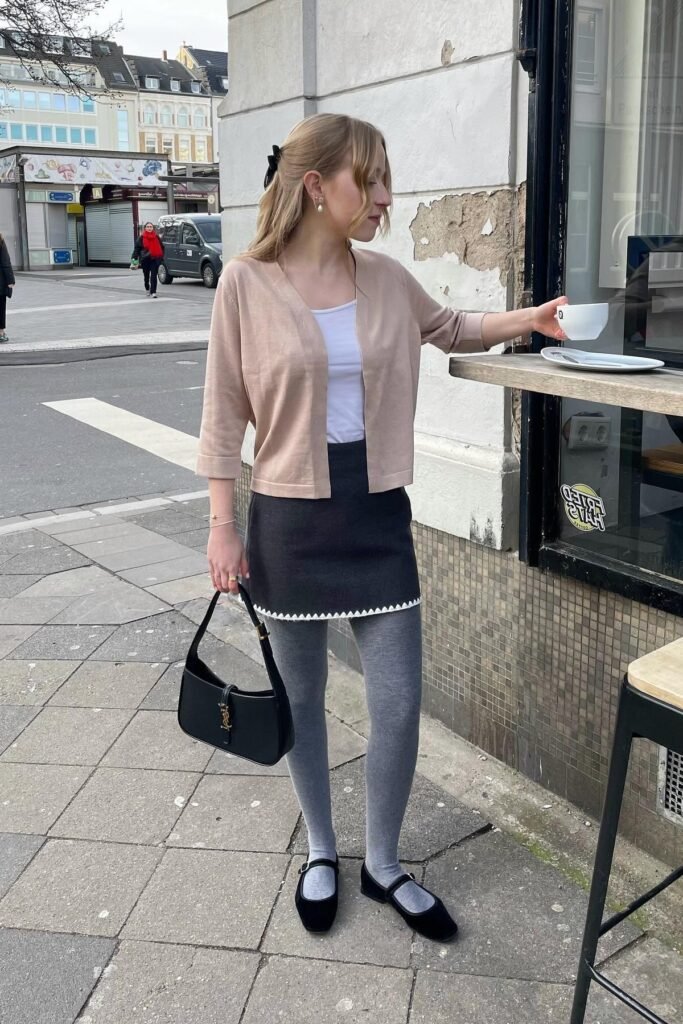Modest and sweet fall brunch outfit: a beige cardigan over a white top, dark grey mini skirt, grey tights, and Mary Jane flats.