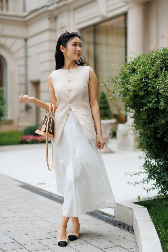 Beige Longline Sleeveless Vest + White Flowy Midi Skirt + Black-Tip Cap-Toe Slingbacks