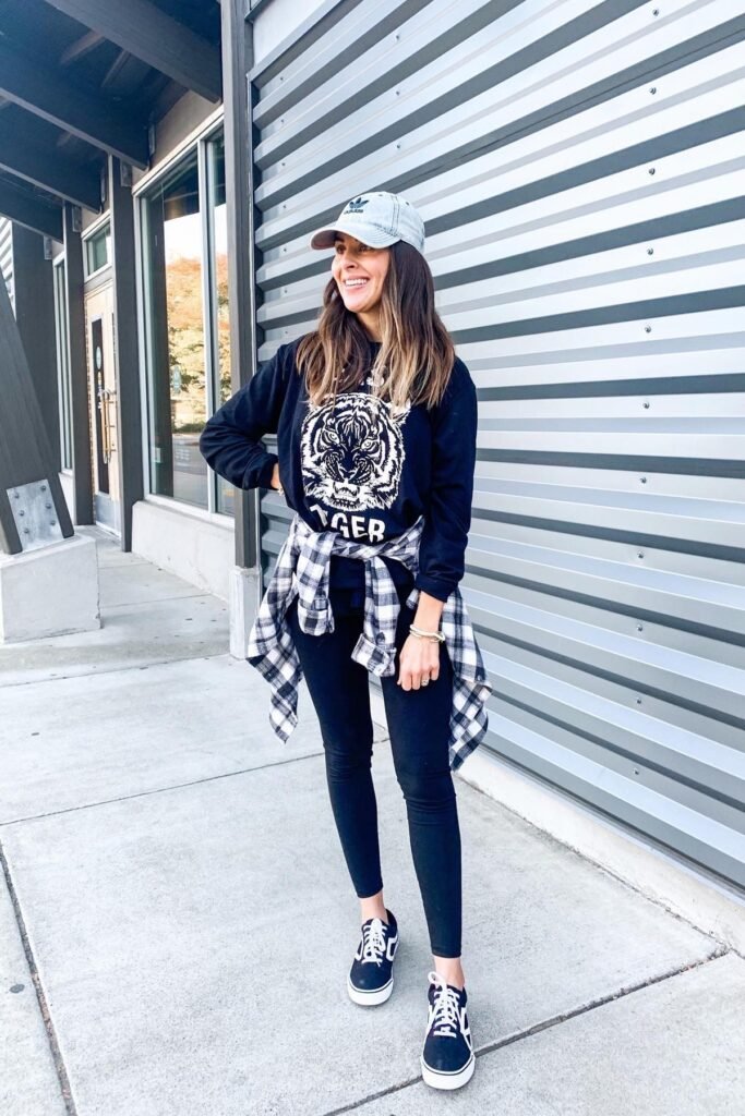 Black Graphic Sweatshirt + Plaid Flannel Shirt (tied at waist) + Black Skinny Leggings + Black Canvas Sneakers + Light Blue Baseball Cap