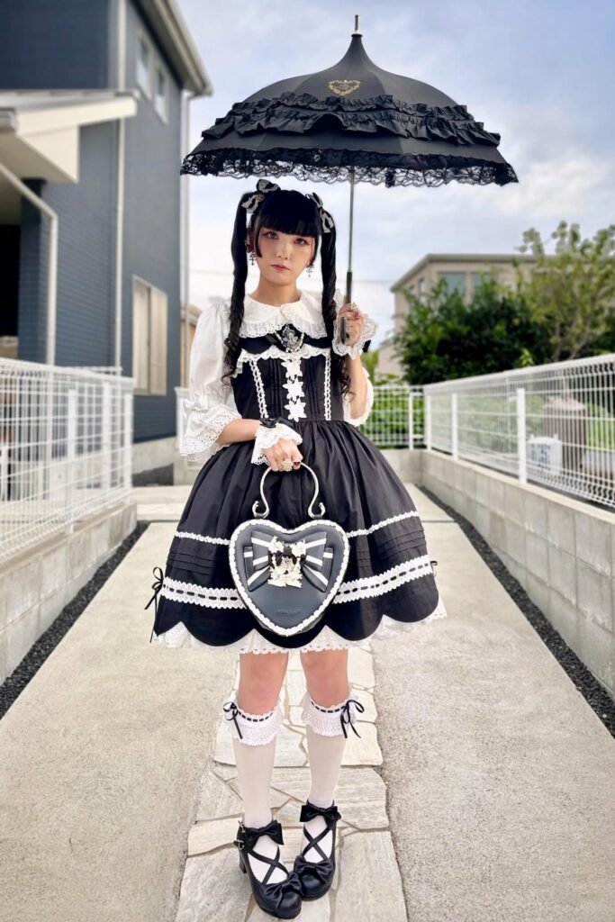 Black Ruffled Jumper Dress + White Puff-Sleeve Blouse + Black Heart-Shaped Bag + Black Bow Heels