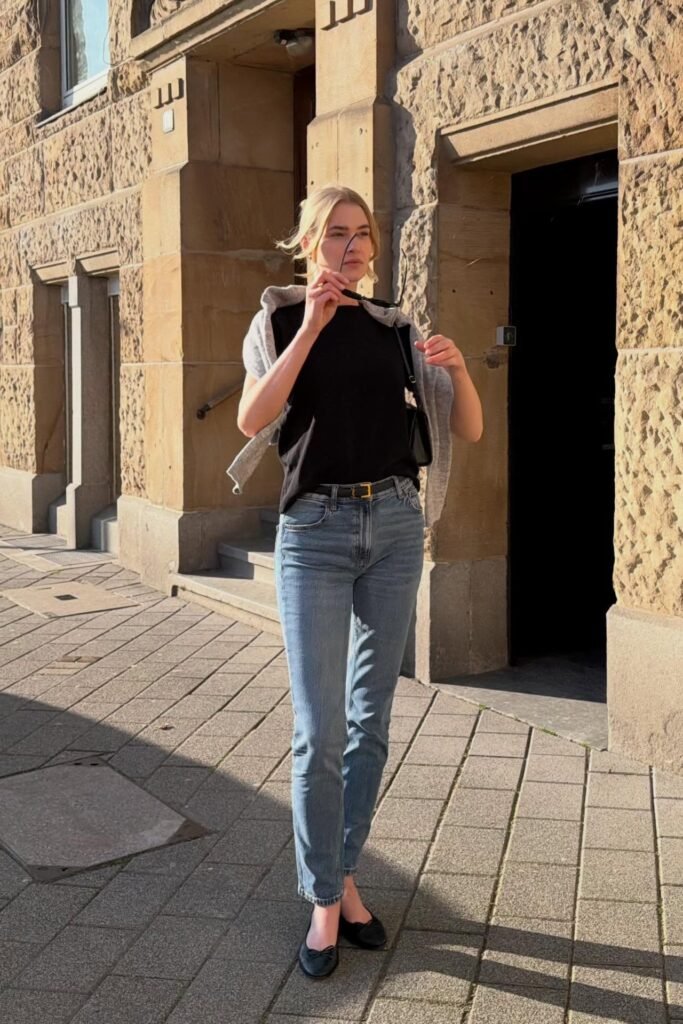 Black T-Shirt + Grey Sweater Over Shoulders + Medium Wash Slim Jeans + Black Ballet Flats