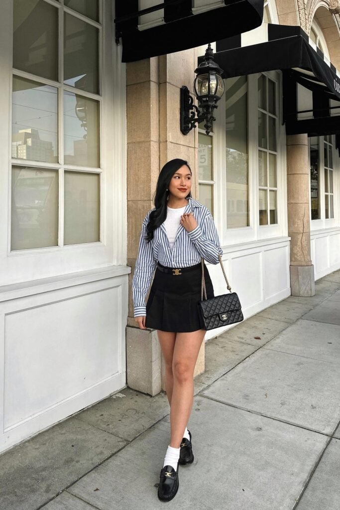 Blue Striped Button-Down Shirt + White Bodysuit + Black Pleated Mini Skirt + Black Loafers