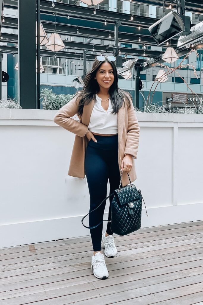 Camel Open-Front Coat + White Cropped Henley + Black High-Waisted Leggings + White Athletic Sneakers + Black Quilted Backpack
