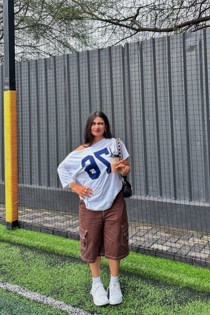Oversized Graphic Off-the-Shoulder Tee + Brown Contrast-Stitch Cargo Shorts + White Crew Socks + White Athletic Sneakers