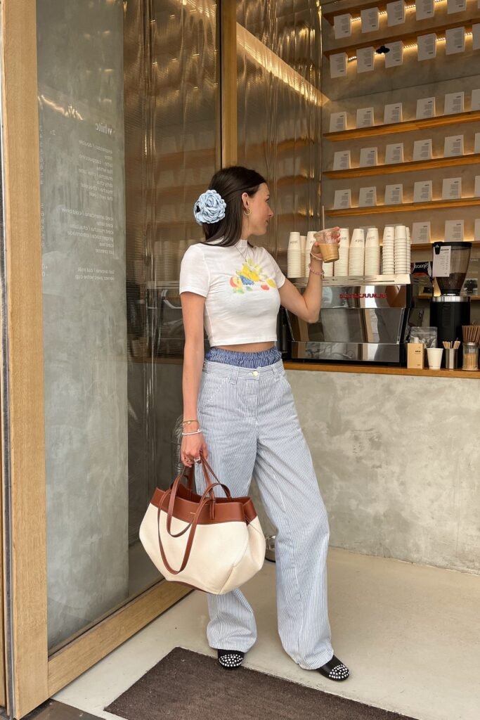 White Graphic Baby Tee + Blue Pinstripe Wide-Leg Trousers + Cream and Brown Tote + Studded Black Flats
