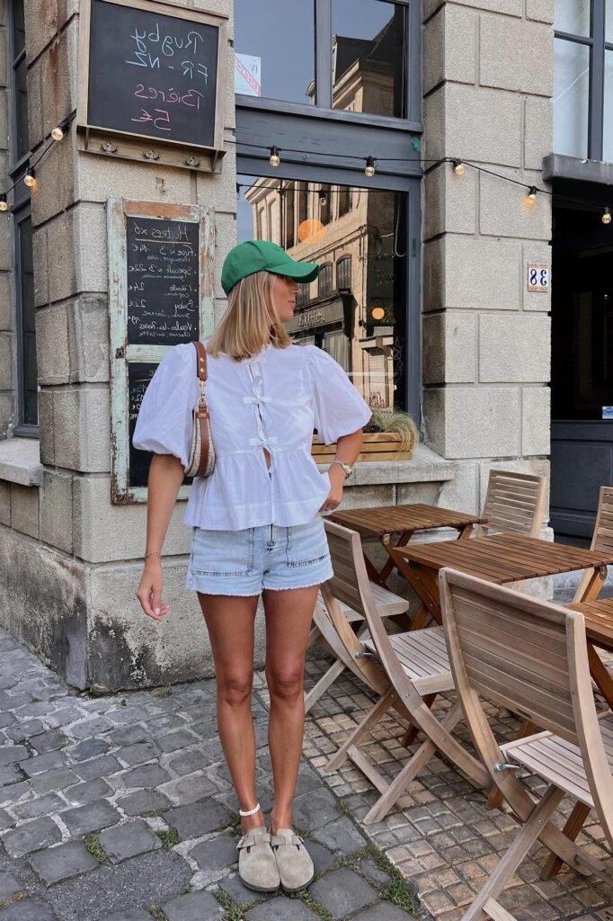 White Puff-Sleeve Bow Blouse + Light Wash Denim Shorts + Green Baseball Cap + Taupe Clogs
