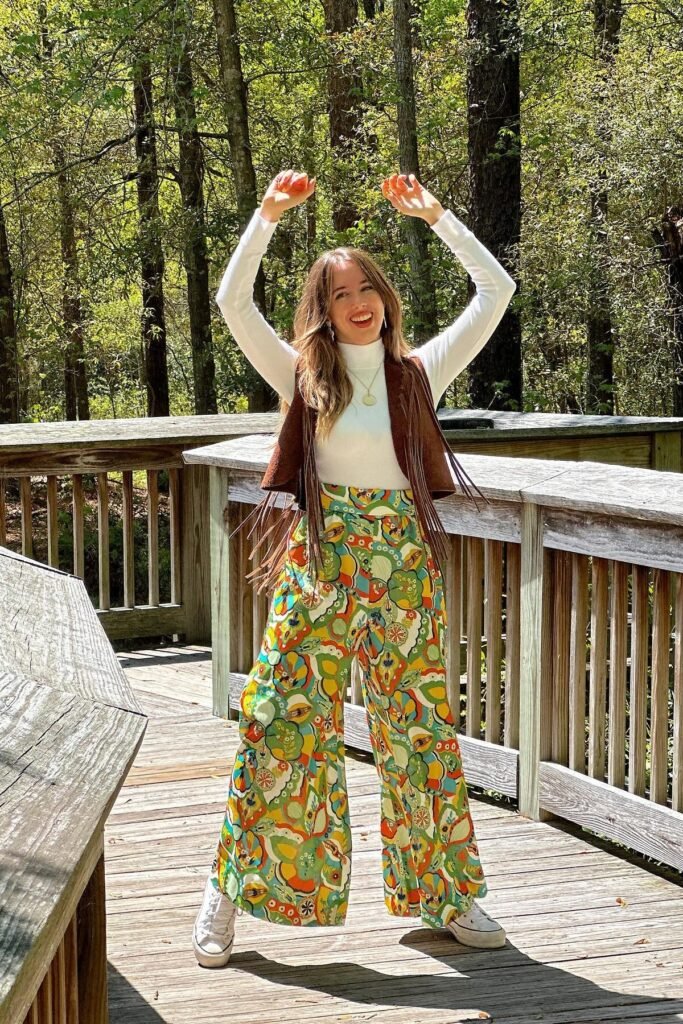 White Turtleneck + Brown Fringe Vest + Psychedelic Print Wide-Leg Pants + White Sneakers