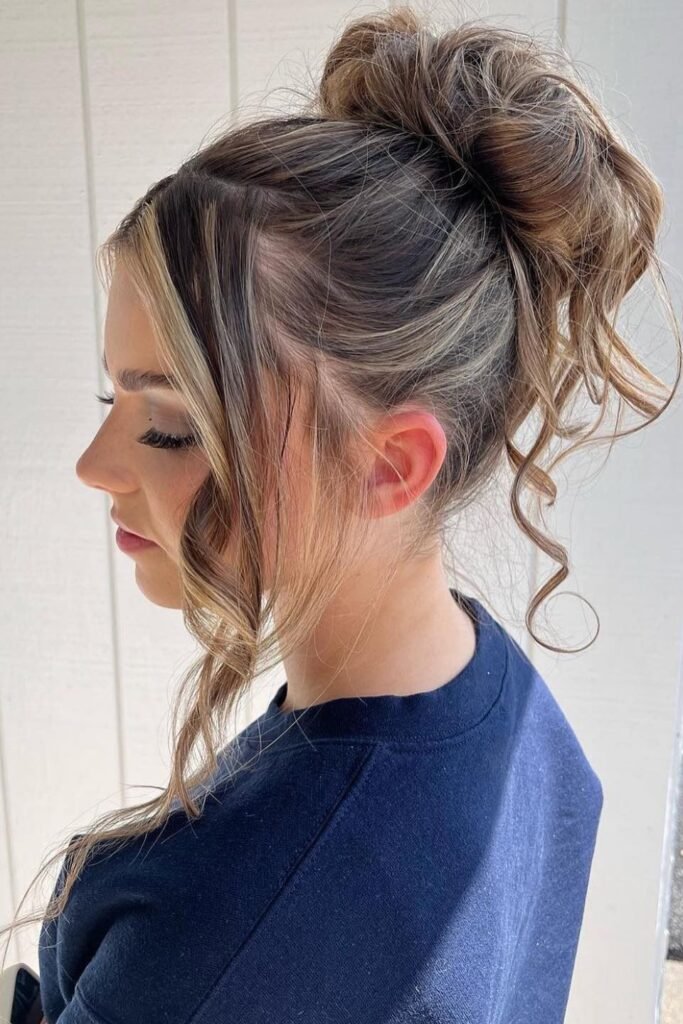 High Messy Bun with Thick Face-Framing Highlights and Tendrils