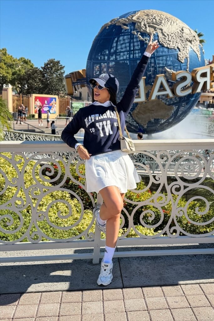 Navy Graphic Sweatshirt + White Pleated Mini Skirt + Silver Sneakers + Navy Baseball Cap