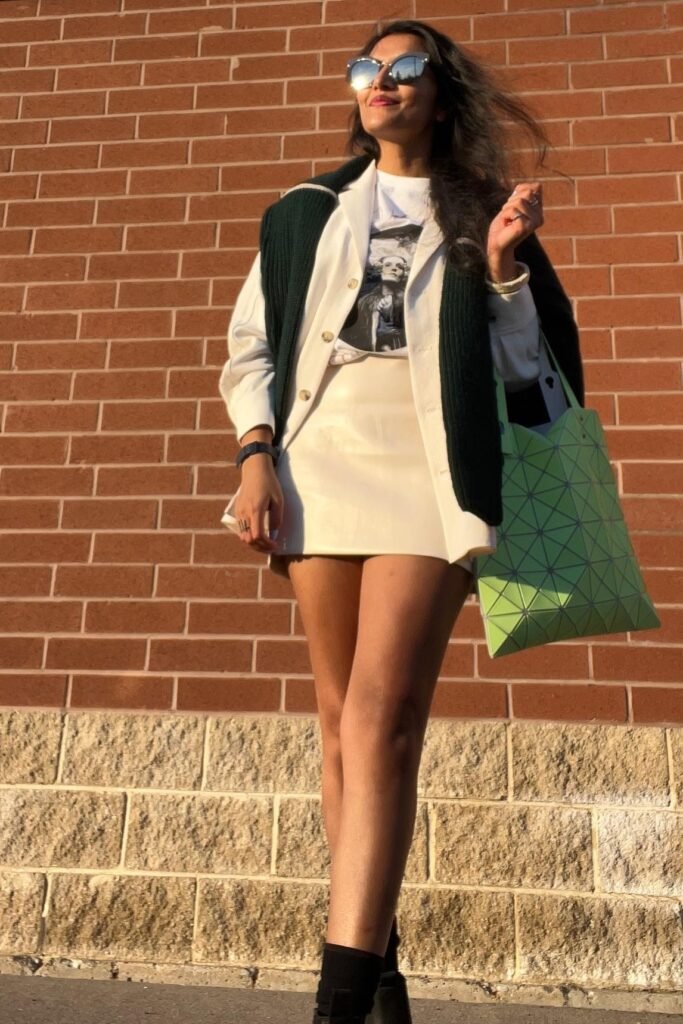 White Button-up Shirt over Graphic Tee + White Mini Skirt + Green Shoulder Sweater